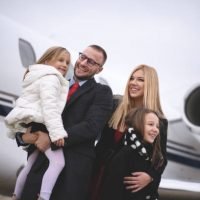 Couple with two daughters in front of private jet airplane at the airport.